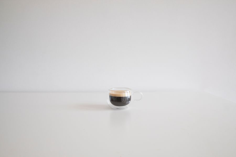 A small glass cup of espresso on a plain white surface.